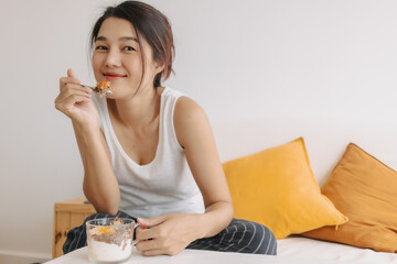 Happy asian woman eating healthy homemade snack made of yogurt.