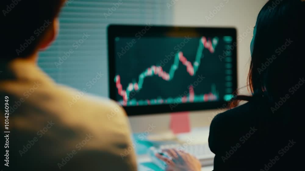 Poster Business professionals working late in the office analyze stock market data displayed on a computer monitor, focusing on charts and graphs to inform investment strategies