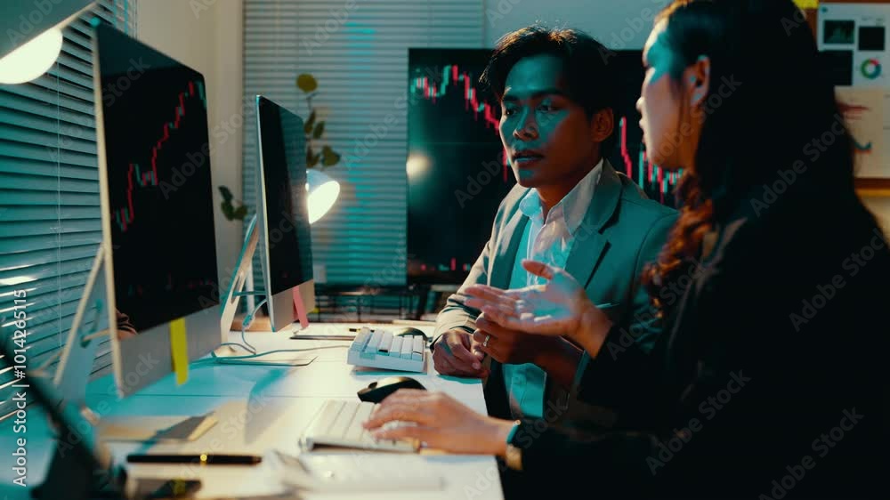 Poster Two stockbrokers engage in a discussion while reviewing stock market data on a computer screen in their office, analyzing charts and graphs to develop investment strategies
