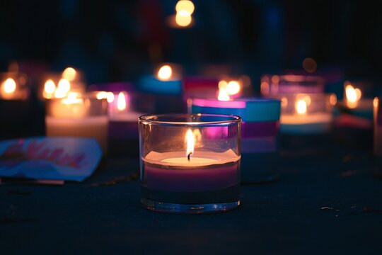 A candlelight vigil commemorating lives lost, illuminated by warm flames and touching tributes against a somber backdrop. - Powered by Adobe