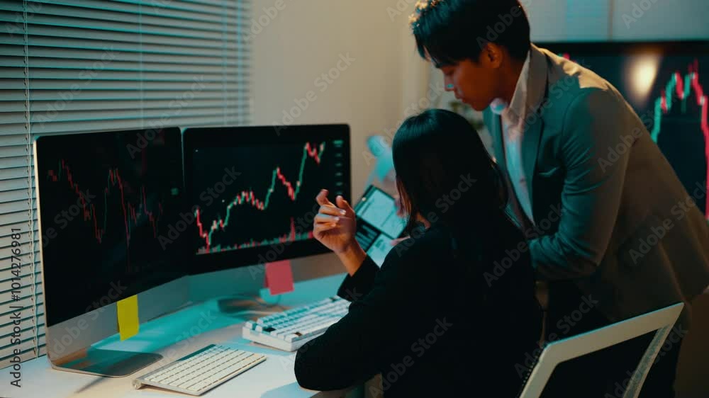 Poster Financial analyst is explaining stock market data to his colleague in the office. He is pointing at the computer screen and showing her a tablet