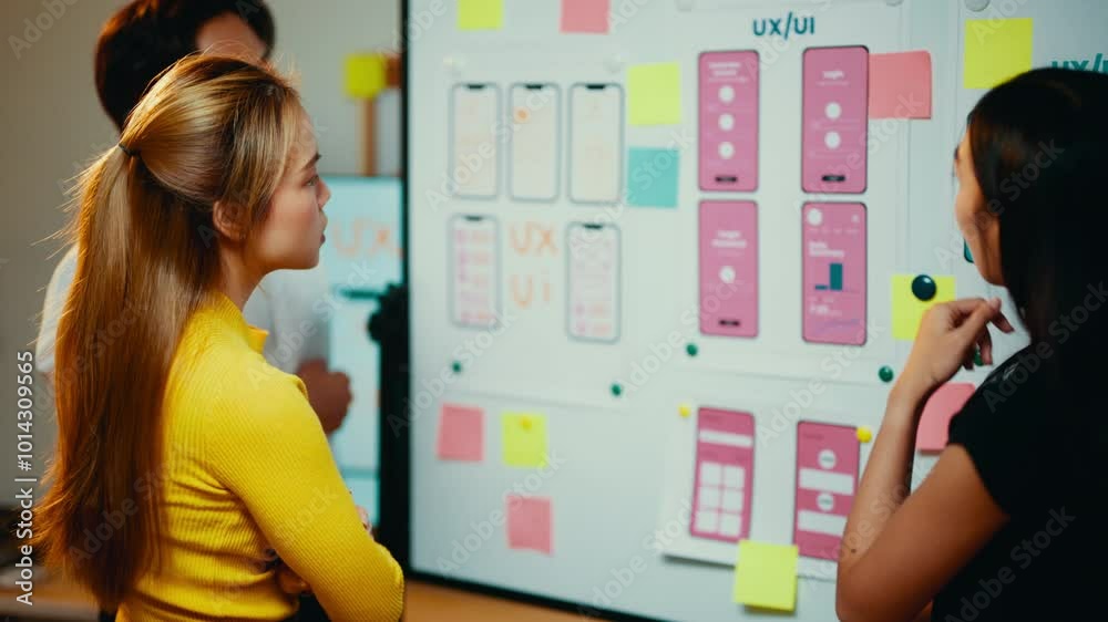 Poster Ux/ui designers are working together in the office. They are discussing the user interface of a mobile application using wireframes and sticky notes