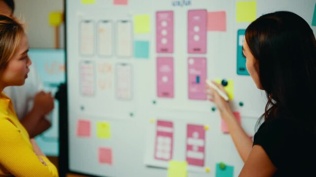 Group of ui and ux designers are collaborating on a mobile application interface, using a whiteboard covered with wireframes and annotations