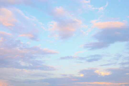 Soft pastel clouds drift across a bright blue sky during early morning or late afternoon in a tranquil landscape.