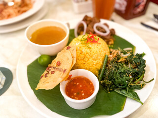 Yellow rice served with vegetables, beef rendang, soup and chili paste.