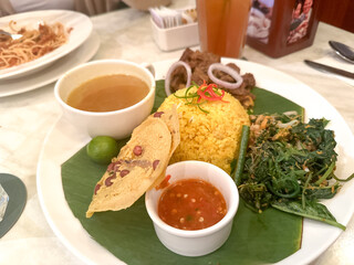 Yellow rice served with vegetables, beef rendang, soup and chili paste.