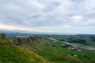 Rolling hills covered with grass leading to the ocean in the distance in New Zealand. The serene countryside is bathed in soft light, with rivers cutting through the valleys below.