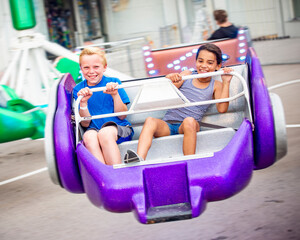 Two diverse kids riding an amusement park ride at the fun theme park. Screaming, laughing and having a great time on a thrilling carnival ride. Intentional motion blur on the image