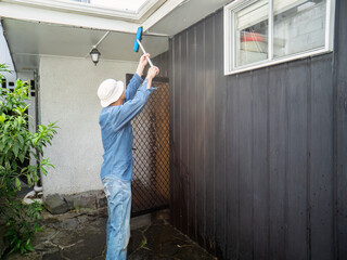 Man cleaning fascia using a brush. Home maintenance work. Auckland.