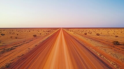 Fototapeta premium Expansive dirt road in a vast desert landscape under a colorful sky at dusk.