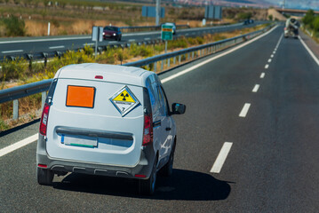 Van with orange ADR license plate and radioactive hazard label, number seven, driving on a motorway.