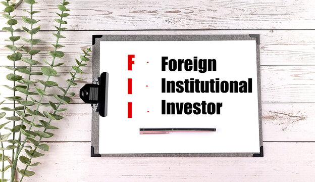 Clipboard with the text foreign institutional investor on a wooden desk with green leaves and a pen 