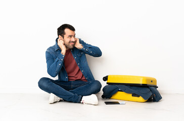 Caucasian handsome man with a suitcase full of clothes sitting on the floor at indoors frustrated...