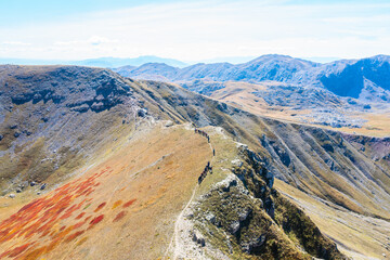 Hikers one behind the other in a hiking line on the ridge of a beautiful mountain during autumn with colorful vegetation - drone aerial shot