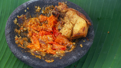 Fried chicken meat and chili sauce in a stone mortar on a banana leaf, focus selected