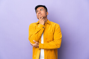 Young Ecuadorian man isolated on purple background having doubts while looking up