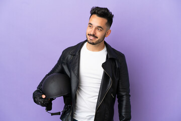 Fototapeta premium Young man with a motorcycle helmet isolated on purple background looking to the side and smiling