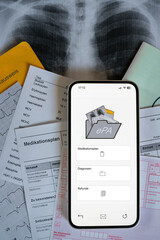 Ein Smartphone auf dem gerade eine elektronische Patientenakte angezeigt wird, liegt auf medizinischen Dokumenten, vertikal   