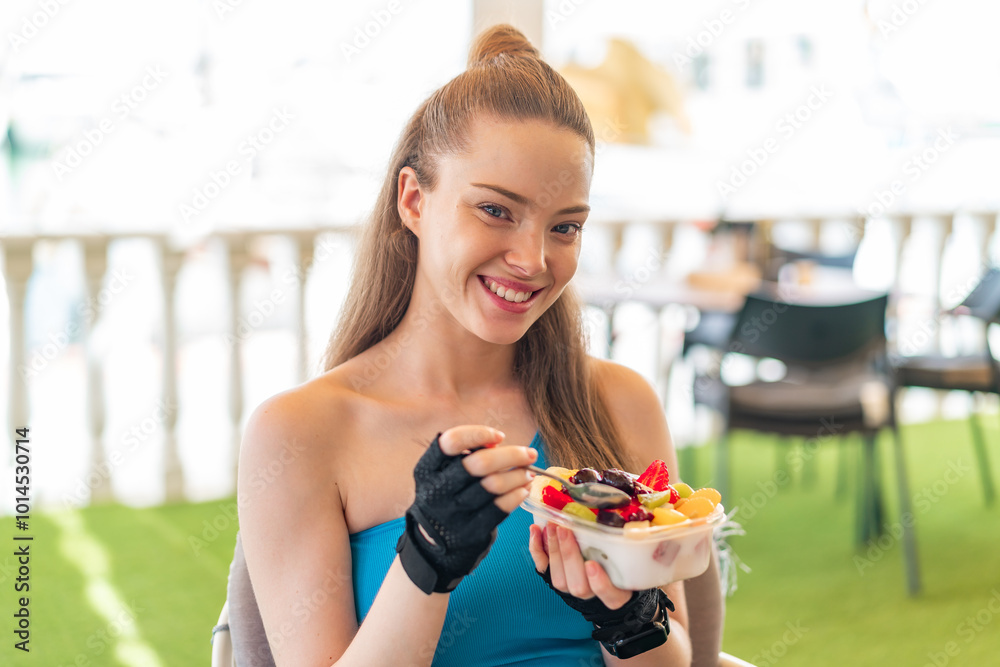 Sticker Young pretty sport girl holding a bowl of fruit at outdoors