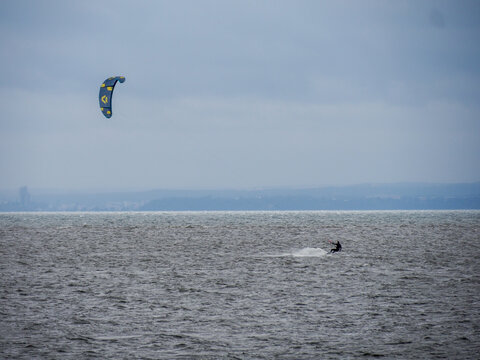 Kitesurfing Against Cloudy Sky and Large Water Body with Visible Shoreline in the Distance