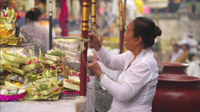 Senior balinese priest or pemangku in white dress purifying offerings with holy water during kuningan ceremony at bali temple