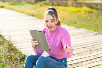 Fototapeta premium Young pretty girl holding a tablet at outdoors surprised and pointing finger to the side