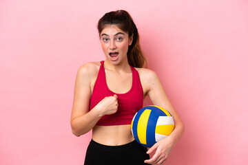 Young caucasian woman playing volleyball isolated on pink background with surprise facial expression