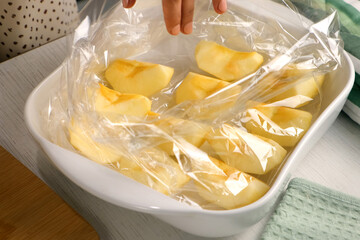 Woman putting apple pieces on ceramic baking sheet to bake in baking sleeve on kitchen, hands close-up. Housewife preparing homemade dish from apples. Culinary, cuisine healthy eating at home.