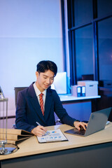 Asian Businessman analyzing reports in a modern office, working on a computer. Perfect for corporate, business, and over time concepts