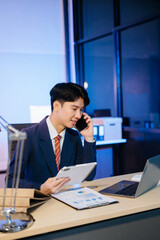 Asian Businessman analyzing reports in a modern office, working on a computer. Perfect for corporate, business, and over time concepts