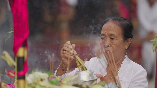 A balinese woman priest sprinkles holy water on offerings to sanctify them during a ceremony at bali temple