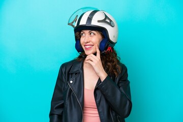 Young caucasian woman with a motorcycle helmet isolated on blue background thinking an idea while looking up