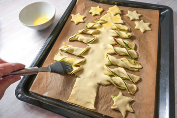 Spreading egg yolk on puff pastry dough filled with homemade pesto and cut in a Christmas tree...
