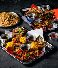Filipino Feast with Grilled Meat, Garlic Fried Rice, grill corn cob, Peri Peri Chicken, Jerk Chicken, Beef Belly Brisket, Pork belly, and Sauces served in tray side view of platter