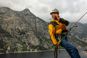 A woman is talking on her cell phone while she is rock climbing