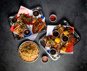 Filipino Feast with Grilled Meat, Garlic Fried Rice, grill corn cob, Peri Peri Chicken, Jerk Chicken, Beef Belly Brisket, Pork belly, Tomato and Sauces served in tray top view of platter