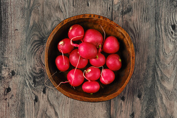 Freshly harvested radishes in a rustic wooden bowl on a weathered wooden surface
