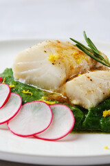 Delicate white fish fillet served on a bed of wilted greens with fresh radish slices and citrus zest