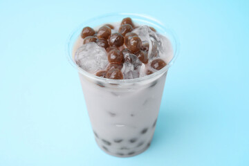 Tasty milk bubble tea in plastic cup on light blue background, closeup