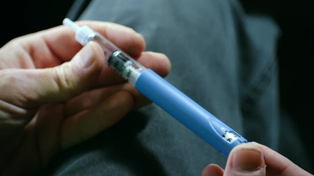 Person diabetic prepares an insulin pen for injection, holding the device in hand while adjusting the dosage. The scene highlights essential steps in diabetes management and treatment