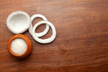 Top view of fresh coconut fruit pieces and coconut shreds in a ceramic pot, isolated on a white background.
