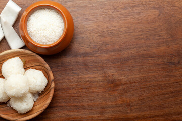 Top view of fresh coconut fruit pieces and coconut shreds in a ceramic pot, with laddu isolated on a white background.