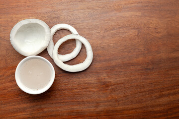 Top view of Fresh coconut fruit with coconut water in a white ceramic bowl, on a wooden background.