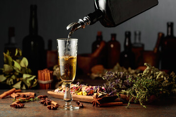 Yellow herbal liquor or mixture is poured from a vintage bottle into a glass.