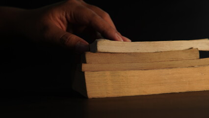 the hand of someone taking an old book. in a dimly lit room. mystery, magic, Halloween, horror, history books.