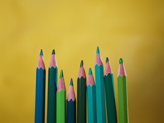 several colored pencils in various green colors on a yellow background