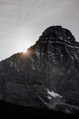 The sun sets behind a rugged mountain peak in Banff National Park, highlighting the rocky textures
