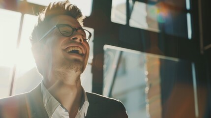 A man with glasses laughs heartily, illuminated by sunlight streaming through a window, creating a warm, joyful atmosphere.