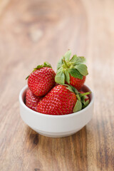 Fresh strawberries in white bowl on wood background with copy space