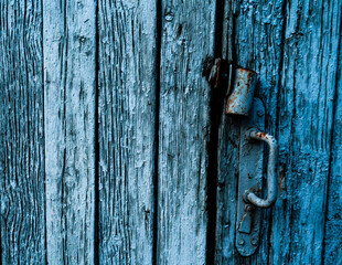 A close-up shot of an old, weathered wooden door with visible peeling paint and a rustic metal handle. The aged texture and blue tones give the image a vintage, distressed look with character.

